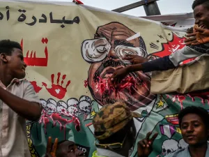 In this file photo taken on April 19, 2019, Sudanese protesters gesture in front of a banner depicting ousted and detained president Omar al-Bashir, during a protest outside the army headquarters in the capital Khartoum. AFP/File