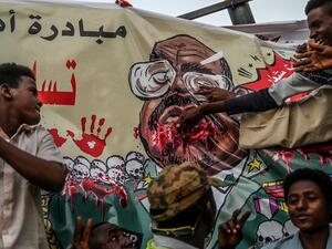 In this file photo taken on April 19, 2019, Sudanese protesters gesture in front of a banner depicting ousted and detained president Omar al-Bashir, during a protest outside the army headquarters in the capital Khartoum. AFP/File