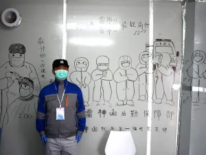 A security personnel stands in front of coronavirus themed drawings seen on a wall at the Leishenshan Hospital that had offered beds for coronavirus patients in Wuhan, in China’s central Hubei province on April 11, 2020. Noel Celis / AFP