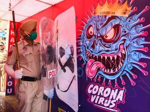 A policeman poses for photos inside a 'disinfectant tunnel' next to a poster depicting the COVID-19 coronavirus during an event in Amritsar on April 16, 2020. Narinder NANU / AFP