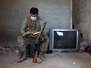 A Turkey-backed Syrian fighter wearing a face mask flips through a book as he rests at a position in the village of Aafes, north of the city of Saraqib in the northwestern Idlib province, during the novel coronavirus pandemic crisis, on April 19, 2020. Abdulaziz KETAZ / AFP