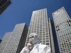 A worker, wearing a protective suit amid concerns about the COVID-19 coronavirus, waits to check the temperature of drivers at the entrance to the car park of a commercial complex in Beijing on April 22, 2020. GREG BAKER / AFP
