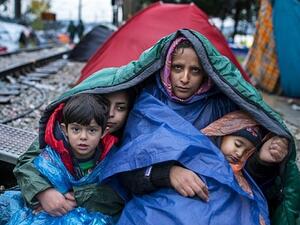 A woman and her children look on as migrants and refugees wait to cross the Greece-Macedonia border in the rain on November 27, 2015 near Gevgelija. (AFP PHOTO / ROBERT ATANASOVSKI)