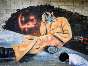 A youth, wearing a protective mask, walks past a mural reading "We are tired" in the Lebanese northern city of Tripoli on April 28, 2020. Lebanon is facing its worst economic crisis since the 1975-1990 civil war, now compounded by a nationwide lockdown to stem the spread of the coronavirus. The Lebanese pound has lost more than half of its value, and prices have soared.This is the case across the country, but Tripoli has been especially hard hit because more than half of its population had already been livi