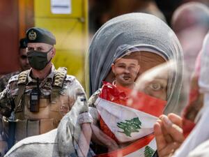This double exposure photo taken on May 3, 2020 shows a Lebanese protester wearing a Lebanese flag face mask as members of the Lebanese Armed Forces stand guard during a demonstration against dwindling economic conditions, at al-Nour Square in the centre of the northern port city of Tripoli. Ibrahim CHALHOUB / AFP