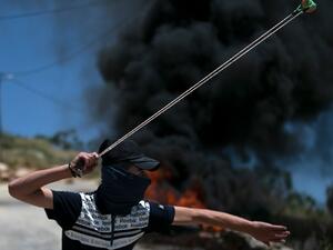 Tires burn as a Palestinian youth uses a sling shot to hurl rocks at Israeli troops, during clashes with them in the West-Bank village of Kfar Qaddum, following a weekly demonstration against the expropriation of Palestinian land by Israel, on May 8, 2020. JAAFAR ASHTIYEH / AFP
