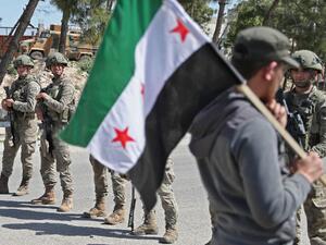 A demonstrator holds a flag of the Syrian opposition as he walks before Turkish soldiers securing a section of the M4 highway, which links the northern Syrian provinces of Aleppo and Latakia, near Ariha in Syria's jihadist-controlled northwestern Idlib province on May 12, 2020. OMAR HAJ KADOUR / AFP