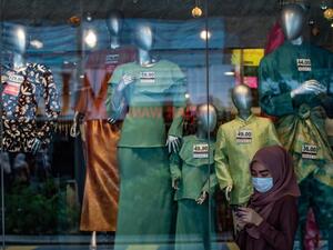 A woman wears a face mask as a preventive measure against the spread of the COVID-19 coronavirus as she browses her phone in front of a shop selling Malaysian cultural outfits called Baju Melayu and Baju Kurung ahead of the Islamic Eid al-Fitr festival, which marks the end of the holy month of Ramadan, in Kuala Lumpur on May 13, 2020. Mohd RASFAN / AFP