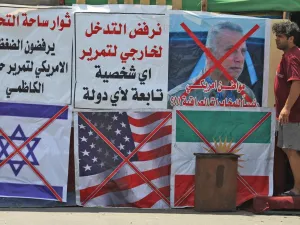 An Iraqi man stands next to the crossed flags of Israel (L), the US and Kurdistan (R) at a protest site along with slogans in Arabic denouncing foreign intervention in Iraq, at Al-Jumhuriyah bridge in the capital Baghdad on May 14, 2020. AHMAD AL-RUBAYE / AFP