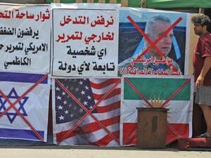 An Iraqi man stands next to the crossed flags of Israel (L), the US and Kurdistan (R) at a protest site along with slogans in Arabic denouncing foreign intervention in Iraq, at Al-Jumhuriyah bridge in the capital Baghdad on May 14, 2020. AHMAD AL-RUBAYE / AFP