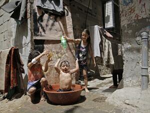 Palestinian girls pour water over a child's head to cool off during a heatwave at Bureij refugee camp in the central Gaza Strip, amidst the COVID-19 pandemic on May 19, 2020. (AFP)
