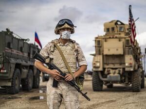 A Russian military police stands next to Russian and US military vehicles along the M4 highway by the town of Tal Tamr on May 25, 2020, as they monitor the reopening of the road to civilian traffic between the border towns of Kobane and Tal Tamr for the first time since a Turkish-backed invasion last year saw the route closed. DELIL SOULEIMAN / AFP