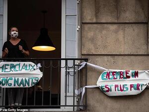 A woman stands on her balcony in Paris behind signs which read 'thank you carers' and 'together we are stronger. (AFP)