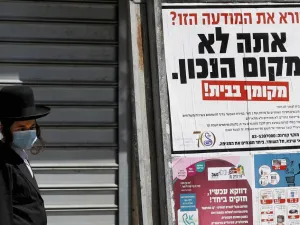 An ultra-Orthodox Jewish man wearing a mask walks past a sign reading in Hebrew "Reading this ad? You're not in the right place. (AFP/File Photo)