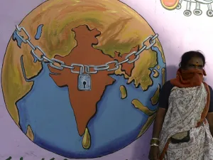 A labourer with her face covered waits for a local transport beside a graffiti depicting a world under lockdown, during a nationwide lockdown as a preventive measure against the COVID-19 coronavirus, on the outskirts of Hyderabad on May 29, 2020. NOAH SEELAM / AFP