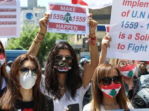 Lebanese anti-government protesters wearing protective gear amid the COVID-19 pandemic lift placards demanding the implementation of United Nations resolutions including the disarmament of armed groups in the country, during a demonstration in the capital Beirut, on May 30, 2020. ANWAR AMRO / AFP