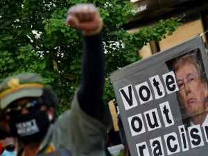 A demonstrator raises his fist in front of a sign calling to vote out racism with a picture of President Donald Trump during a peaceful protest against police brutality and the death of George Floyd, on June 7, 2020 in Washington, DC. Olivier DOULIERY / AFP