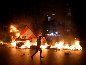 A protester holding the Lebanese flag runs as protesters block the Jounieh Tripoli highway with flaming tires set aflame during a demonstration against dire economic conditions in Jal el Dib North East of the Lebanese capital Beirut late on June 11, 2020. The Lebanese pound sank to a record low on the black market on June 11 despite the authorities' attempts to halt the plunge of the crisis-hit country's currency, money changers said. Lebanon is in the grips of its worst economic turmoil in decades, and hol