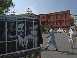 People wearing facemasks cross a street beside an auto-rickshaw with a graffiti depicting actor Heath Ledger (L) in his role as the Joker, in Rawalpindi on June 26, 2020.  Aamir QURESHI / AFP