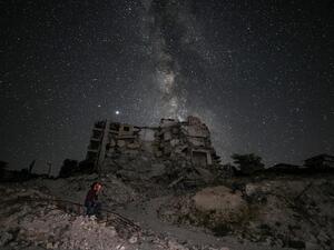 This long-exposure picture taken early on June 27, 2020 shows a man smoking past buildings destroyed by prior bombardment in the town of Ariha in Syria's rebel-held northwestern Idlib province, as the Milky Way galaxy is seen in the night sky above. Omar HAJ KADOUR / AFP