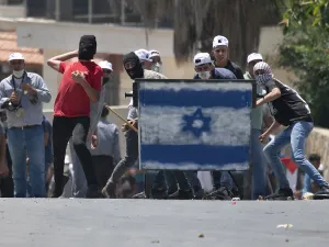 Palestinian protesters, standing behind a shield painted with the colours of the Israeli flag, hurl stones towards Israeli troops (unseen) during a demonstration in the village of Kfar Qaddum in the occupied West Bank against the Jewish state's plans to annex part of the Palestinian territory on July 3, 2020. Rival Palestinian factions Fatah and Hamas pledged the previous day a united campaign against Israel's prospective plans to annex territory in the occupied West Bank, in a rare joint press conference, 
