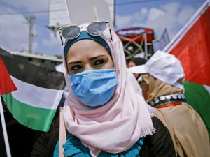 A Palestinian woman wearing a protective mask amid the COVID-19 pandemic lifts a national flag during a rally for supporters of the Fateh movement against Israel's West Bank annexation plans, in Beit Hanun in the north of the Gaza Strip, on July 6, 2020. MOHAMMED ABED / AFP