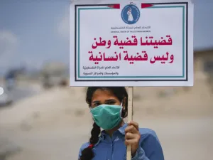 A Palestinian girl wearing a protective mask amid the COVID-19 pandemic lifts a placard which reads "Our cause that of a homeland, not a humanitarian one", during a rally for supporters of the Fateh movement against Israel's West Bank annexation plans, in Beit Hanun in the north of the Gaza Strip, on July 6, 2020. Mohammed ABED / AFP