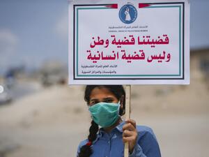A Palestinian girl wearing a protective mask amid the COVID-19 pandemic lifts a placard which reads "Our cause that of a homeland, not a humanitarian one", during a rally for supporters of the Fateh movement against Israel's West Bank annexation plans, in Beit Hanun in the north of the Gaza Strip, on July 6, 2020. Mohammed ABED / AFP