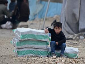 In this file photo a displaced Syrian boy sits next to humanitarian aid, consisting of heating material and drinking water, at a camp in the town of Mehmediye, near the town of Deir al-Ballut along the border with Turkey, on February 21, 2020. Rami al SAYED / AFP