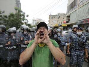 A protester wearing a scarf of the Shiite movement Hezbollah chants slogans while being flanked by Lebanese police during an anti-US demonstration near the United States' Embassy headquarters in Awkar, northeast of the capital Beirut on July 10, 2020. JOSEPH EID / AFP
