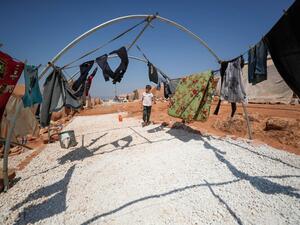 A displaced Syrian boy stands next to clothes at a camp for displaced Syrians from Idlib and Aleppo provinces, near the town of Maaret Misrin in Syria's northwestern Idlib province on July 11, 2020. The Idlib region, Syria's last major opposition bastion, is home to some three million people, nearly half of whom have been displaced from other regions. OMAR HAJ KADOUR / AFP