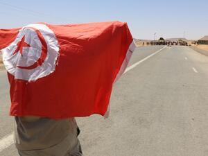 A man waves a national flag in front of Tunisian army soldiers gathered on July 12, 2020, at the border post with neighbouring Libya near the southern town of Dehiba, during a protest by Tunisians expressing their anger after the death earlier this week of a young man who according to demonstrators was killed by the military,  FATHI NASRI / AFP