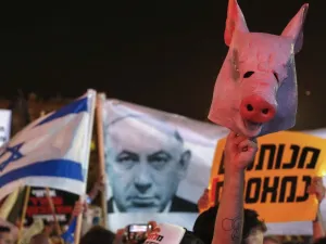 An Israeli protester lifts a mask in the shape of a pig's head during a demonstration in Rabin Square in the central coastal city of Tel Aviv, on July 11, 2020, to protest the government's abandonment of the country's self-employed and other sectors after forcing their businesses to close under COVID-19 regulations, according to the organizers. JACK GUEZ / AFP
