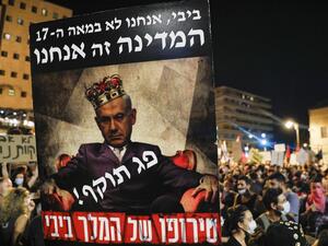 A poster is raised showing Israeli Prime Minister Benjamin Netanyahu wearing a crown and a line across his chest reading in Hebrew "expired" above another line reading "the madness of King Bibi", and other text (top) reading "Bibi we are not in the 17th century, we are the state" during a demonstration against the Israeli government near the Prime Minister's residence in Jerusalem on July 25, 2020. Ahmad GHARABLI / AFP