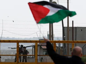 A Palestinian protester waves his national flag in front of Israeli security forces outside the compound of the Israeli-run Ofer prison near Betunia in the Israeli-occupied West Bank, March 30, 2016. (AFP Photo)