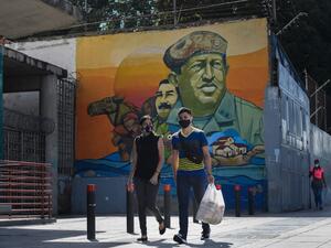 People wearing protective masks walks past a mural depicting Venezuela's late President Hugo Chavez, in downtown Caracas on July 28, 2020, after the government intensified a nationwide lockdown as a preventive measure against the spread of COVID-19. Federico PARRA / AFP