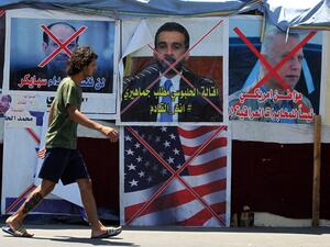 An Iraqi anti-government demonstrator walks past posters of Iraqi polititians and a US flag in Tahrir Square in the capital Baghdad, on August 1, 2020. Iraq will hold its next parliamentary elections nearly a year early, the premier announced yesterday, as he seeks to make good on promises he offered when he came to power. Protests began in October, with thousands taking to the streets of Baghdad and across the south. Demonstrators demanded that the political system be dismantled, pointing to endemic corrup