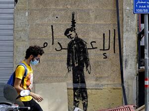A Lebanese volunteer walks past graffiti depicting a hanged politician with the word "execution", in the devastated Beirut neighbourhood of Gemmayzeh, on August 11, 2020, following a huge chemical explosion that ravaged large parts of the capital. JOSEPH EID / AFP
