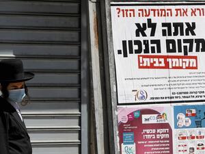 In this file photo taken on April 03, 2020 an ultra-Orthodox Jewish man wearing a mask walks past a sign reading in Hebrew "Reading this ad? You're not in the right place. Your place is at home", in the religious Israeli city of Bnei Brak, near Tel Aviv. (AFP/File Photo)