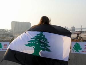 A woman, draped in a black-striped Lebanese flag, looks at the site of the massive explosion at Beirut's port area, during a demonstration to mark one month since the cataclysmic August 4 explosion that killed 191 people, in the Lebanese capital Beirut on September 4, 2020. The explosion piled on new misery for Lebanese already reeling from the coronavirus pandemic and the country's worst economic crisis in decades. As well as killing more than 190 people, the explosion injured at least 6,500 and left 300,0
