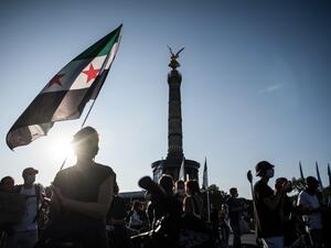 A protester holds an old Syrian flag during a demonstration for the evacuation of all migrant camps in Greece after the fire at the Moria refugee camp on Lesbos, on September 20, 2020 in Berlin. STEFANIE LOOS / AFP