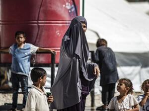 A woman partially covers her face as she stands by children near a water cistern at Camp Roj, housing family members of people accused to belong to the Islamic State (IS) group who were relocated from al-Hol camp, in the countryside near al-Malikiyah (Derik) in Syria's northeastern Hasakah province on September 30, 2020. Delil SOULEIMAN / AFP