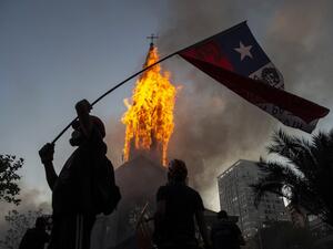 A demonstrator flutters a Chilean flag outside the burning church of Asuncion, set on fire by protesters, on the commemoration of the first anniversary of the social uprising in Chile, in Santiago, on October 18, 2020, as the country prepares for a landmark referendum. MARTIN BERNETTI / AFP