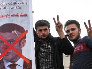 Men flash the victory gesture as they pose for a picture next to a sign condemning French President Emmanuel Macron, and depicting him with a pig snout, for his comments over Prophet Mohammed cartoons in Syria's rebel-held northwestern city of Idlib on October 25, 2020. OMAR HAJ KADOUR / AFP