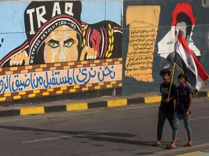 Iraqi youths carry a national flag as they walk past a mural painting in the capital Baghdad's Tahrir Square on October 28, 2020, during a cleanup operation by security forces allowing roads around the city centre, the scene of anti-government protests, to reopen. AHMAD AL-RUBAYE / AFP