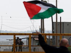 A Palestinian protester waves his national flag in front of Israeli security forces outside the compound of the Israeli-run Ofer prison near Betunia in the Israeli occupied West Bank, March 30, 2016. (AFP Photo)