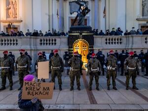 A woman holds a sign reading "You have blood on your hands" near military police and riot police officers standing guards in front of believers praying on the stairs of the Holy Cross Church as protesters take part in demonstration against tightening Poland's already restrictive abortion law, in Warsaw on October 30, 2020. (AFP)