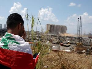 A man draped in a Lebanese flag stands before the ravaged port of Beirut. AFP