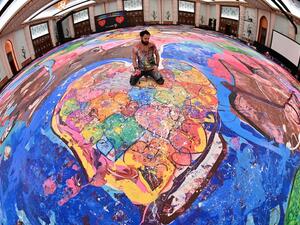 A picture taken with fisheye lens shows contemporary British artist Sacha Jafri sitting on his record-breaking painting entitled 'The Journey of Humanity'. AFP