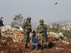 Israeli soldiers detain a Palestinian protester as an Israeli settler hurls rocks at Palestinians during a demonstration against the expansion of settlements in the occupied-West Bank town of Salfit, near the Israeli settlement of Ariel, on November 30, 2020. JAAFAR ASHTIYEH / AFP